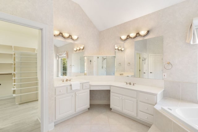 full bath featuring a relaxing tiled tub, a walk in closet, vaulted ceiling, and vanity