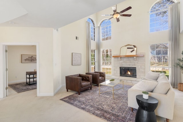 living room with visible vents, a ceiling fan, a towering ceiling, a stone fireplace, and carpet floors