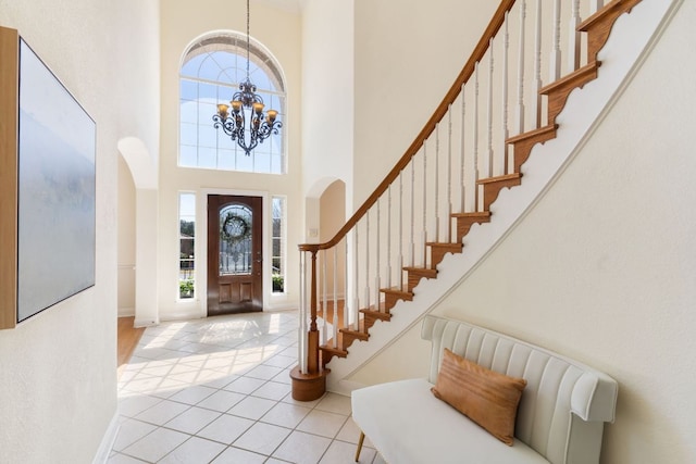 foyer entrance with tile patterned flooring, a high ceiling, baseboards, stairway, and an inviting chandelier