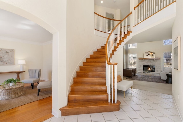 staircase with baseboards, tile patterned flooring, a high ceiling, crown molding, and a fireplace