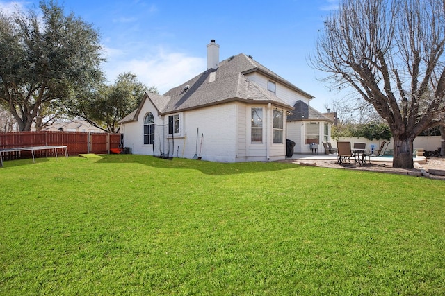 rear view of property featuring a patio, a fenced backyard, a chimney, a trampoline, and a yard