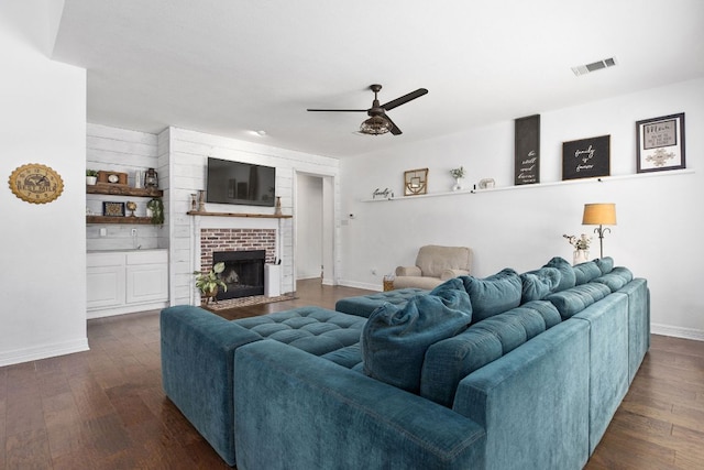 living area featuring baseboards, visible vents, ceiling fan, dark wood-type flooring, and a fireplace