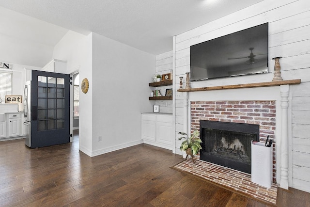 living area featuring a textured ceiling, a fireplace, dark wood finished floors, and baseboards