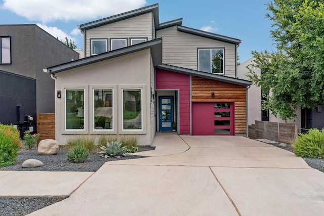 contemporary home with a garage, fence, concrete driveway, and stucco siding