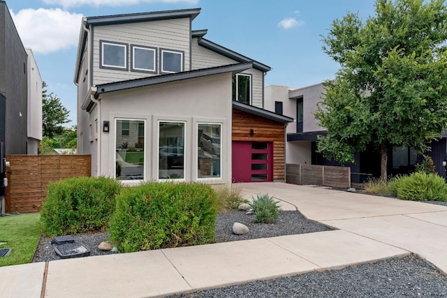 contemporary house with a garage, concrete driveway, fence, and stucco siding