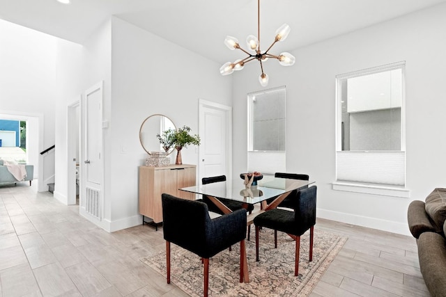 dining space featuring light wood finished floors, baseboards, a towering ceiling, stairs, and a notable chandelier