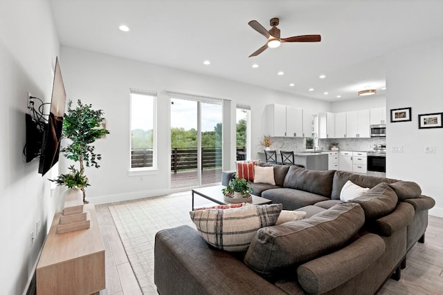 living area with baseboards, a ceiling fan, light wood-style flooring, and recessed lighting