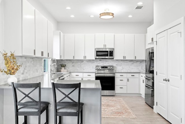 kitchen featuring stainless steel appliances, visible vents, a sink, a peninsula, and a kitchen breakfast bar