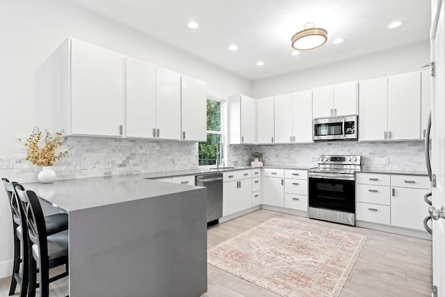 kitchen with stainless steel appliances, decorative backsplash, white cabinetry, a sink, and a peninsula