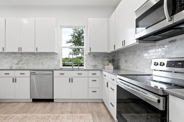 kitchen with backsplash, light wood-style flooring, appliances with stainless steel finishes, white cabinets, and a sink