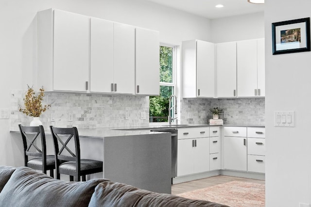 kitchen featuring light wood finished floors, light countertops, decorative backsplash, white cabinets, and a sink