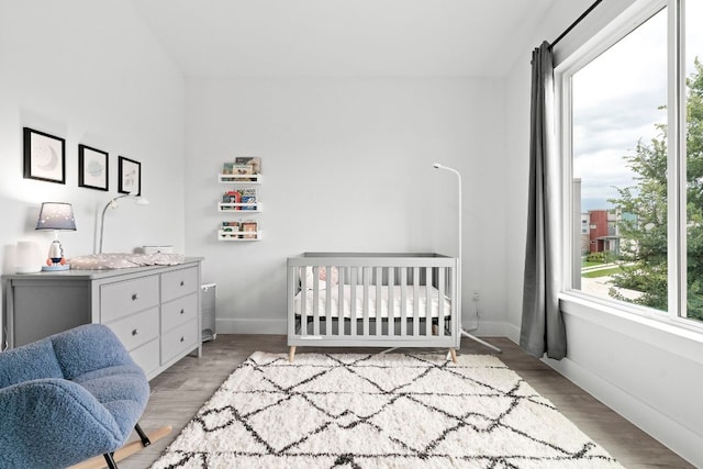 bedroom with baseboards, a crib, and light wood-style floors