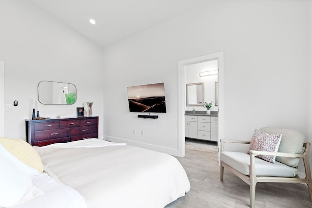 bedroom with baseboards, a wall unit AC, ensuite bath, light wood-style floors, and recessed lighting