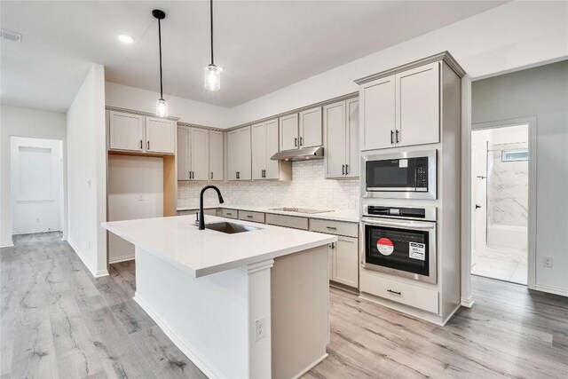148 Rocky View Ln, Georgetown, TX 78628 - kitchen with appliances with stainless steel finishes, under cabinet range hood, light wood-style floors, backsplash, and a center island with sink