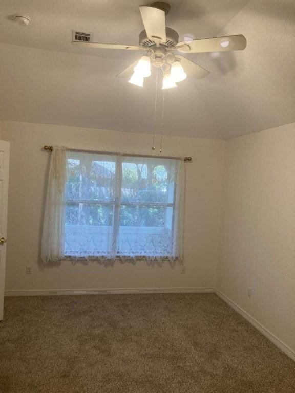 spare room featuring lofted ceiling, carpet, visible vents, and a ceiling fan