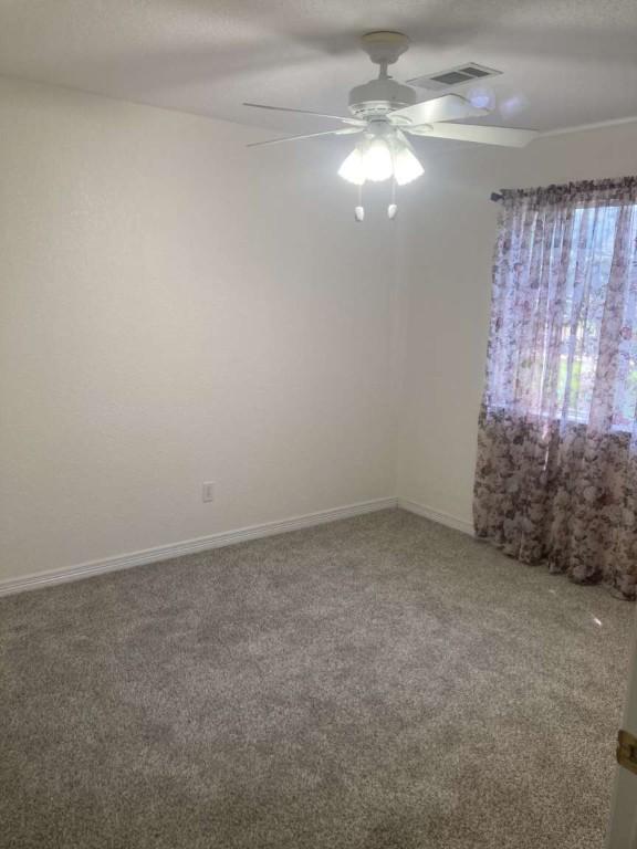 spare room with carpet, visible vents, ceiling fan, and baseboards