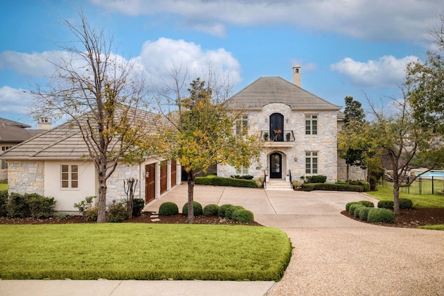 french country home featuring a garage, concrete driveway, stone siding, a chimney, and a front lawn