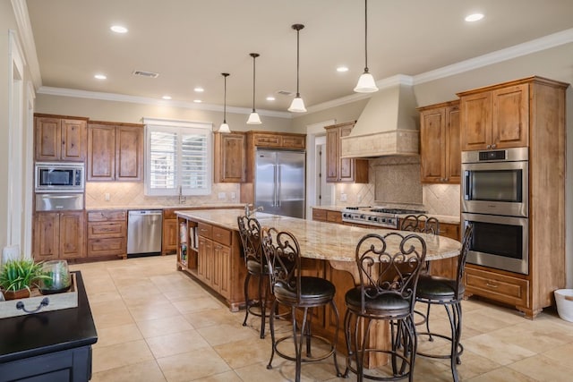 kitchen with a large island, visible vents, brown cabinetry, built in appliances, and premium range hood