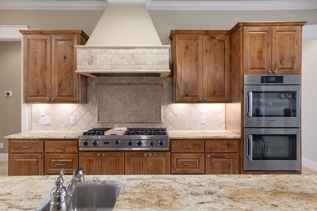 kitchen with appliances with stainless steel finishes, custom range hood, crown molding, and light stone countertops