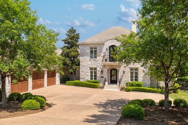 french country home featuring concrete driveway, a chimney, stone siding, and a garage