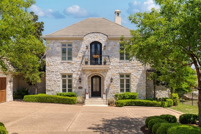 french country inspired facade with a chimney, a balcony, and stone siding