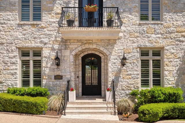 view of exterior entry featuring a balcony and stone siding