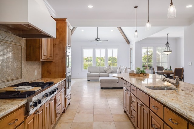 kitchen with ceiling fan, brown cabinetry, stainless steel gas cooktop, a sink, and custom range hood