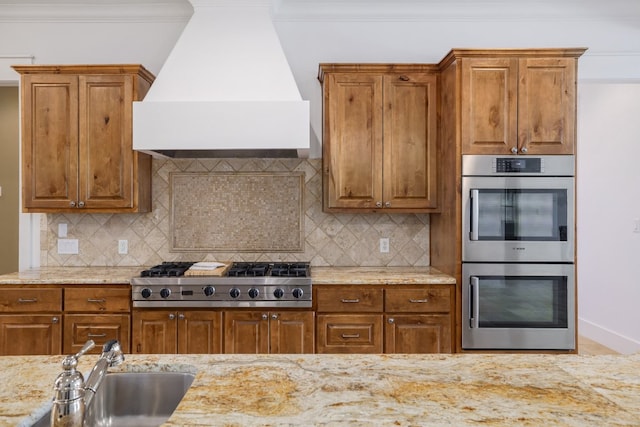 kitchen featuring a sink, appliances with stainless steel finishes, brown cabinets, and premium range hood