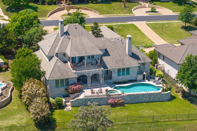back of property with a fenced backyard, a chimney, a balcony, and stone siding