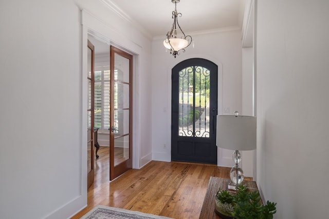 foyer featuring crown molding, light wood-style floors, arched walkways, french doors, and baseboards
