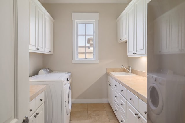 clothes washing area with cabinet space, a sink, separate washer and dryer, baseboards, and light tile patterned floors