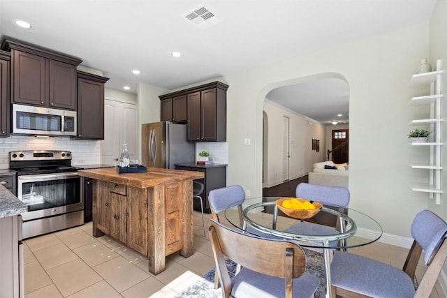 kitchen with arched walkways, light tile patterned floors, visible vents, wooden counters, and appliances with stainless steel finishes