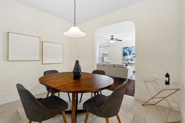 dining space with light tile patterned floors, baseboards, arched walkways, and a ceiling fan