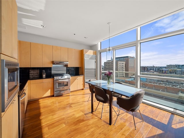 kitchen featuring appliances with stainless steel finishes, expansive windows, a view of city, under cabinet range hood, and light brown cabinets