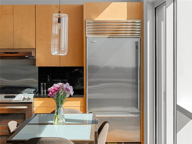 kitchen with dark countertops, under cabinet range hood, stainless steel appliances, and backsplash