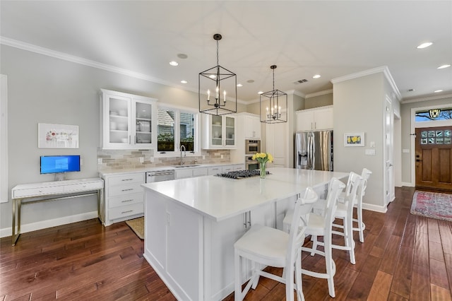 kitchen with stainless steel appliances, a sink, white cabinetry, backsplash, and a center island