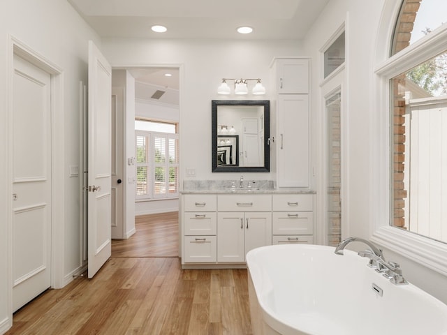 full bath featuring recessed lighting, a soaking tub, vanity, wood finished floors, and baseboards