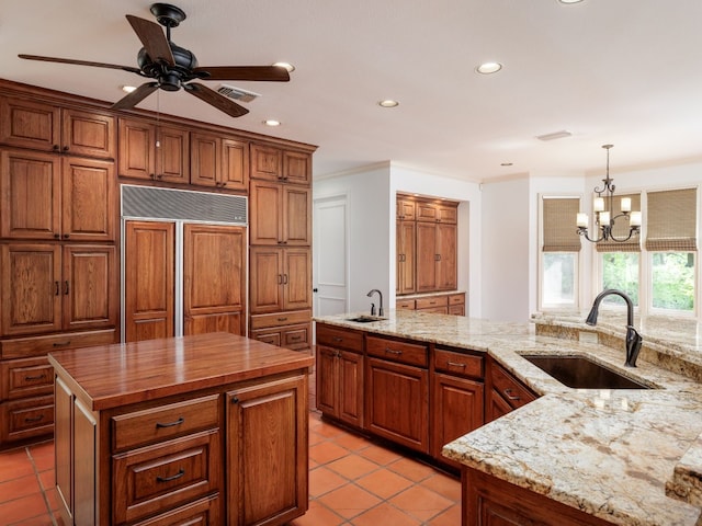 kitchen with light tile patterned floors, brown cabinetry, a kitchen island, paneled built in refrigerator, and a sink