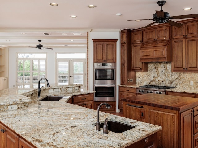 kitchen with appliances with stainless steel finishes, a spacious island, a sink, and wood counters