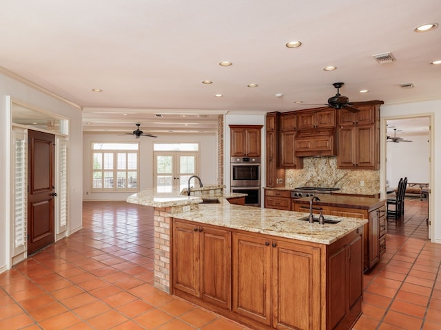 kitchen featuring stainless steel appliances, a large island with sink, decorative backsplash, and a sink