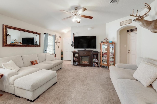 living area featuring visible vents, arched walkways, a glass covered fireplace, lofted ceiling, and light colored carpet