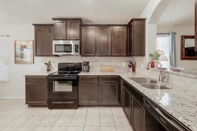 kitchen featuring dark brown cabinetry, light stone counters, a sink, black appliances, and backsplash