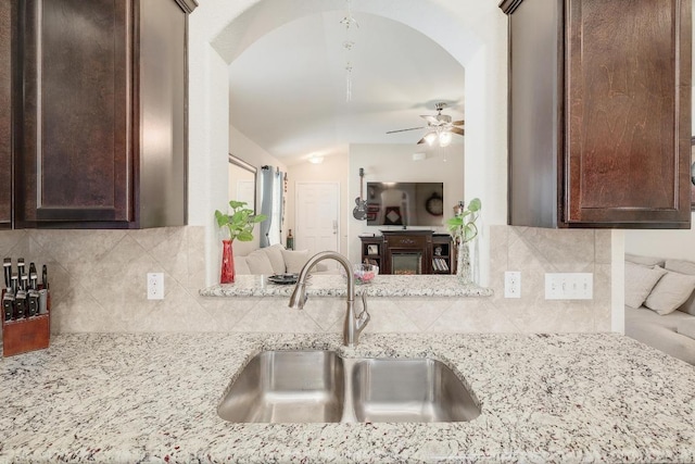 kitchen with tasteful backsplash, a ceiling fan, light stone countertops, dark brown cabinets, and a sink