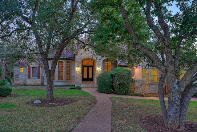 view of front facade with stone siding, french doors, and a front lawn