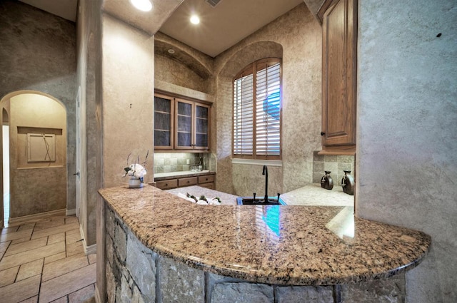 kitchen with arched walkways, light stone counters, a sink, decorative backsplash, and stone tile flooring