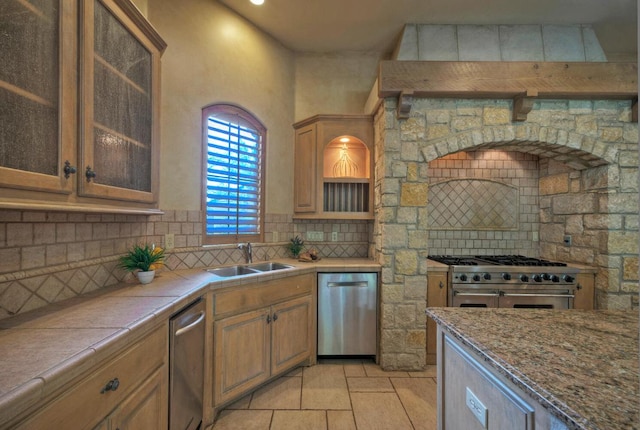 kitchen featuring tile countertops, glass insert cabinets, a sink, stainless steel appliances, and backsplash