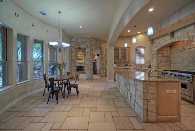 kitchen with light stone counters, visible vents, high end stainless steel range oven, glass insert cabinets, and a sink