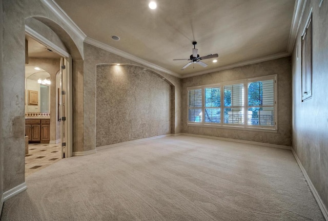 empty room with ornamental molding, arched walkways, light colored carpet, and ceiling fan