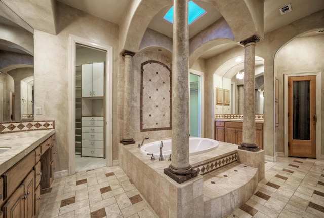 full bathroom with a garden tub, stone tile floors, two vanities, visible vents, and decorative columns