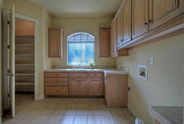 kitchen with light countertops, brown cabinetry, a sink, and baseboards